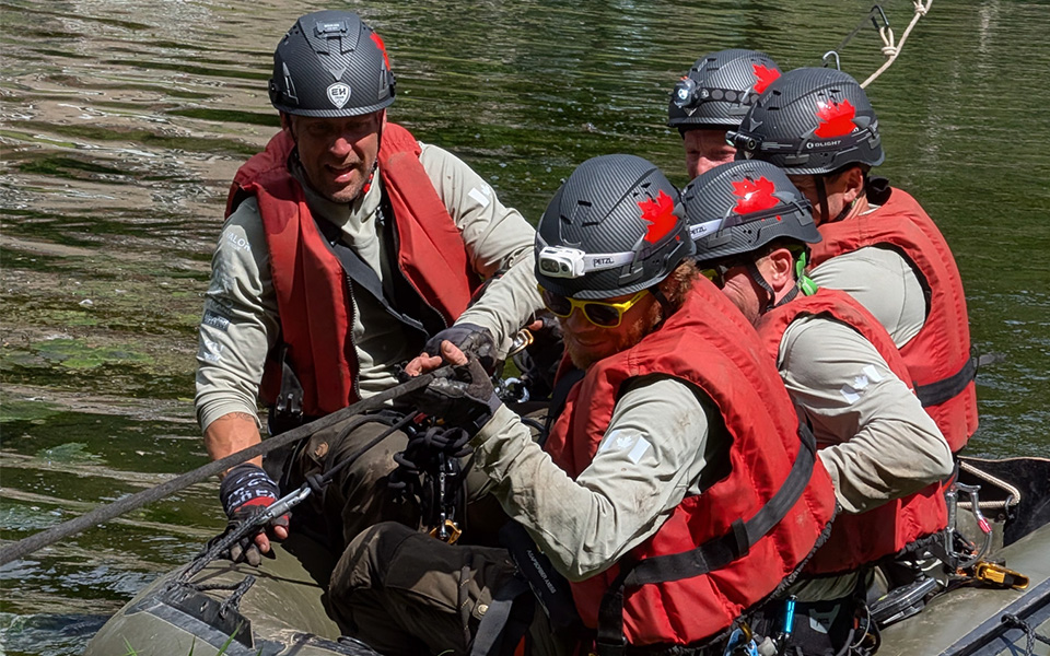 Rescue team members wearing helmets and red safety gear during a technical rope rescue operation.